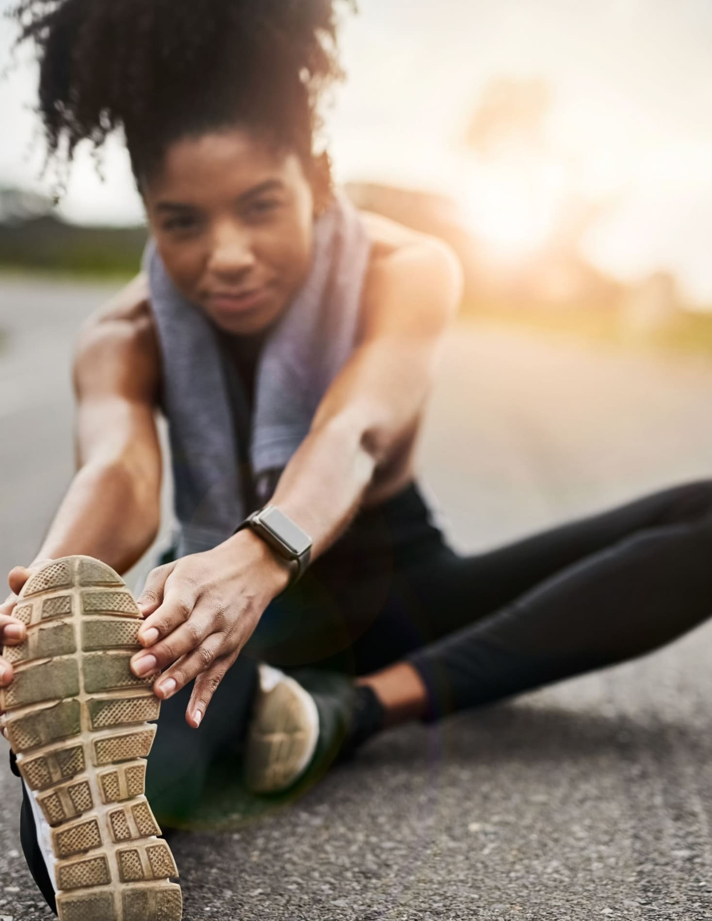 A woman in athletic wear stretching on the ground during outdoor exercise at sunset.