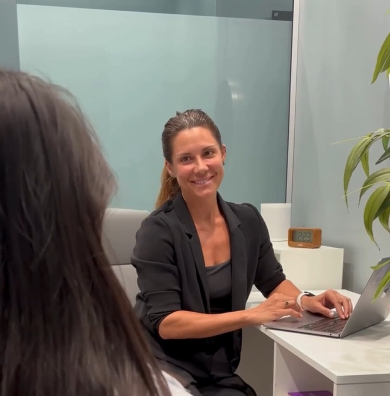 A provider at a table smiling while working on a laptop in an office setting.