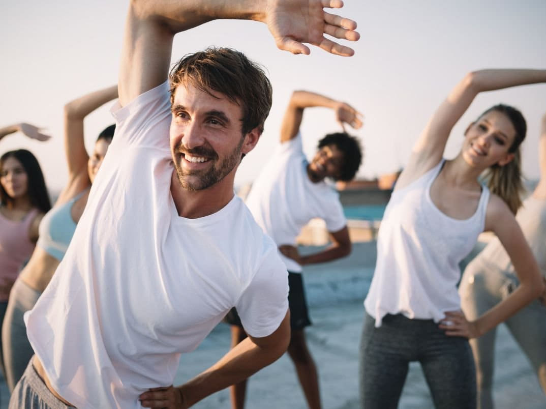 A group of people taking part in outdoor yoga and stretching on a rooftop at sunset.